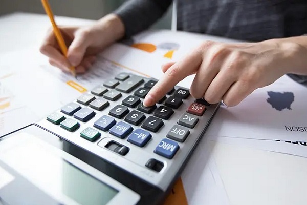 دست فرد در حال محاسبه هزینه ثبت شرکت در عمان با استفاده از ماشین حساب و مدارک مالی